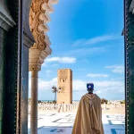 Guard soldier in national costume at the entrance of Mausoleum of Mohammed V and square with Hassan tower in Rabat on sunny day. Location: Rabat, Morocco, Africa