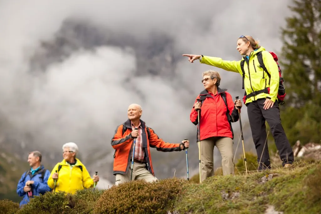 Tour guide hiking young female hiking guide showing senior group surrounding mount